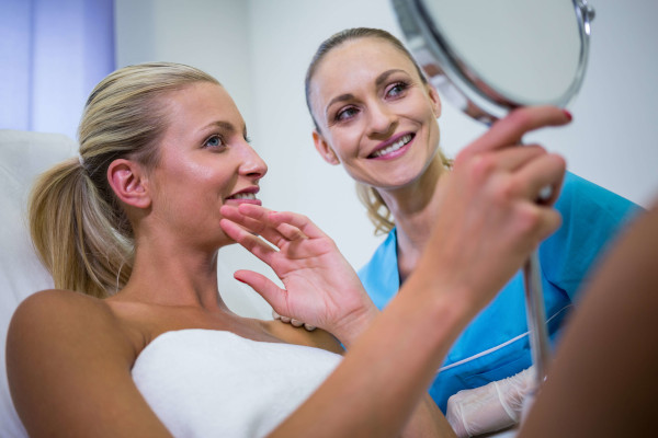 woman checking her skin in the mirror after receiving cosmetic treatment